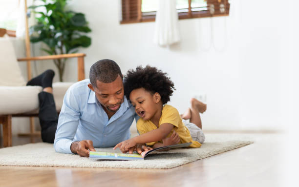 African American Father and his son lying reading book on the floor stock photo