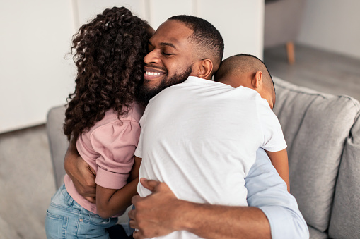 Happy Loving Family. Portrait of cheerful smiling African American dad embracing his little children, expressing love. Girl, boy and man hugging, enjoying time together, celebrating Father's day