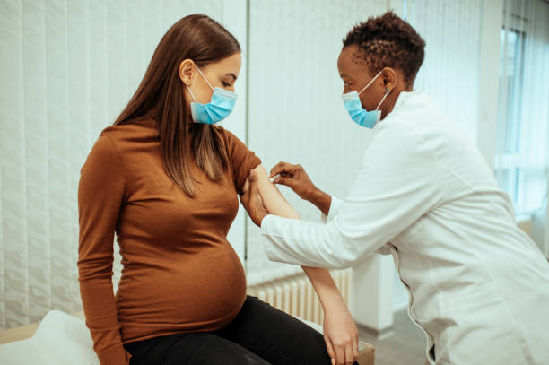 afrikaanse amerikaanse vrouwelijke arts die een zwangere vrouw voor vaccinatie voorbereidt - arts vrouw mondkapje stockfoto's en -beelden