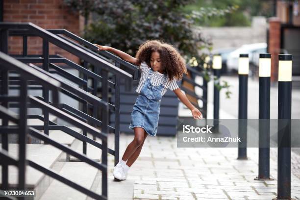 African american kid girl walks down steps on city street. Portrait of child in denim skirt and T-shirt outdoors