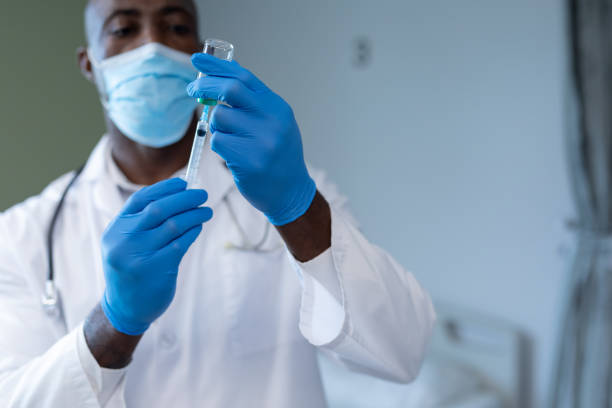yüz maskesi ve eldiven takan afrikalı amerikalı erkek doktor covid aşısı hazırlıyor - south africa covid stok fotoğraflar ve resimler