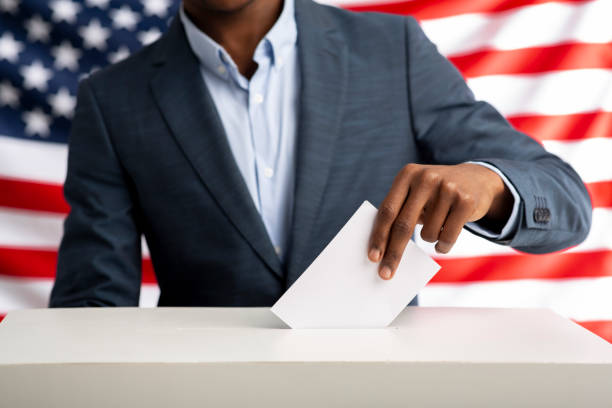 African american man holds envelope in hand above vote ballot Election or referendum in America. African american man holds envelope in hand above vote ballot. USA flag on background. election stock pictures, royalty-free photos & images