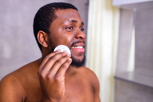 african american man looking at himself in the bathroom mirror squeezing pimple stock photo