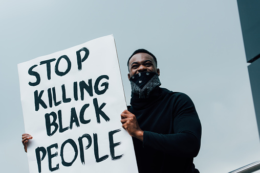 african american man with scarf on face holding placard with stop killing black people lettering outside