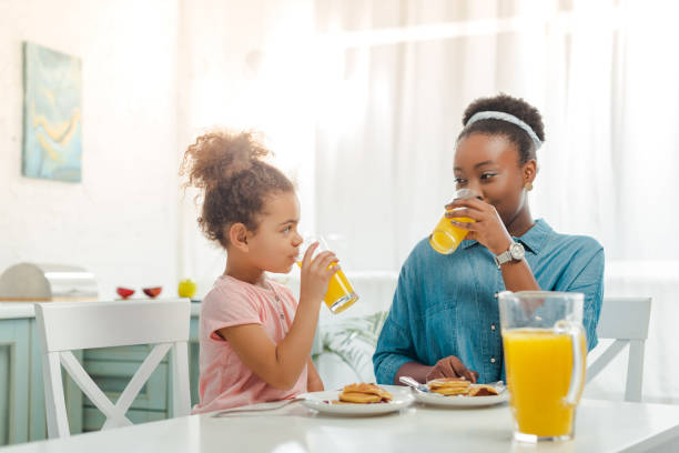 african american mother and daughter drinking orange juice near tasty pancakes african american mother and daughter drinking orange juice near tasty pancakes juice drink stock pictures, royalty-free photos & images