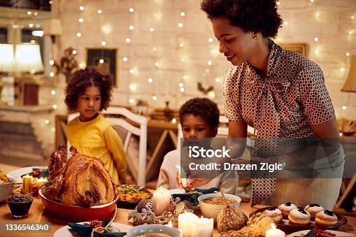 istock African American mother lights candles during Thanksgiving meal at dining table. 1336546340