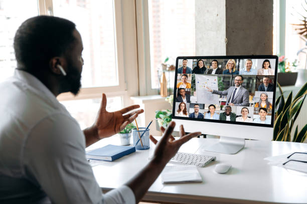 African American successful man, ceo, manager, consultant, holding an online business conference, with multiracial employees, sitting at their desk at home, gesturing hands, discuss about strategy stock photo