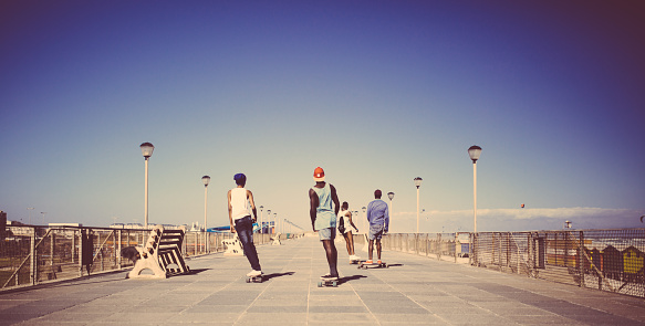 Cool group of African American teenagers casually longboarding together on a walkway down at the beach