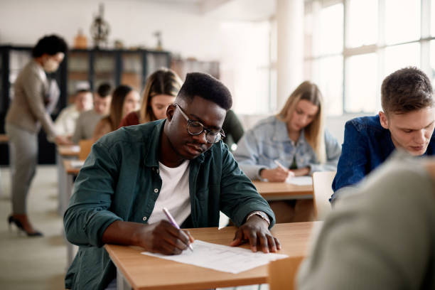 African American university student writing while having test in the classroom. Black male student and his classmates writing during exam at the university. Cuirz stock pictures, royalty-free photos & images