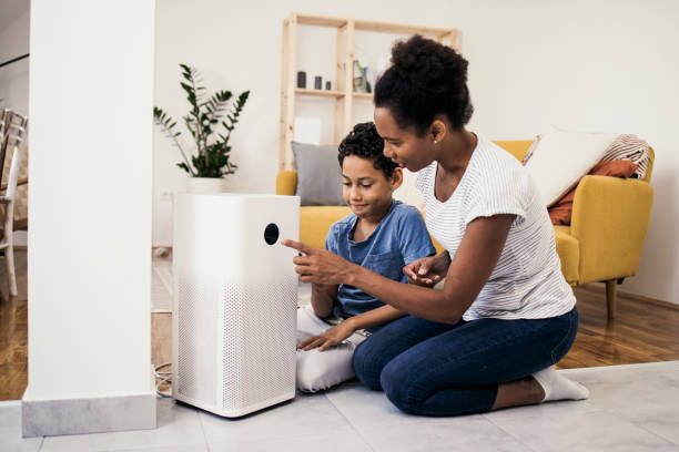 African American woman and her son adjusting a home air cleaner using a smart system stock photo
