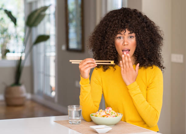 African american woman eating asian rice at home cover mouth with hand shocked with shame for mistake, expression of fear, scared in silence, secret concept African american woman eating asian rice at home cover mouth with hand shocked with shame for mistake, expression of fear, scared in silence, secret concept how do you say shut up in japanese stock pictures, royalty-free photos & images