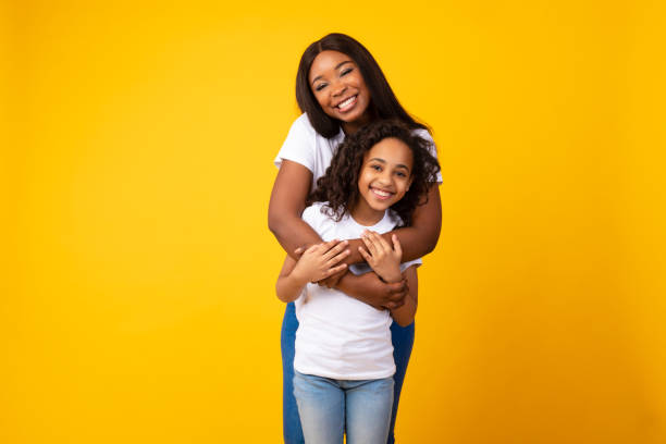 african american woman hugging her smiling daughter from the back - black mother imagens e fotografias de stock