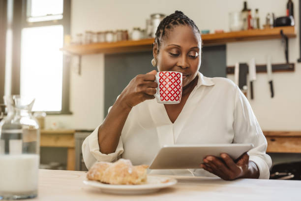 afro-amerikaanse vrouw met een tablet tijdens het ontbijt thuis - africa cup stockfoto's en -beelden