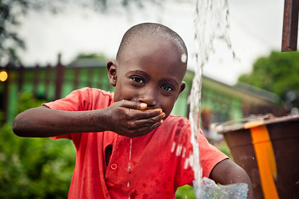 african boy by water pump - africa cup stockfoto's en -beelden
