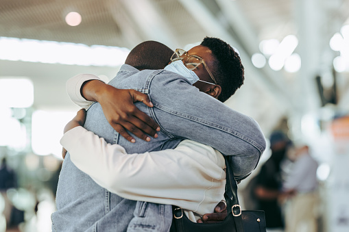 Man hugging woman during pandemic at airport terminal. African couple reuniting at airport arrivals.