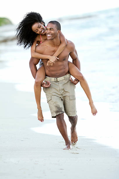 African ethnicity couple piggybacking on beach stock photo
