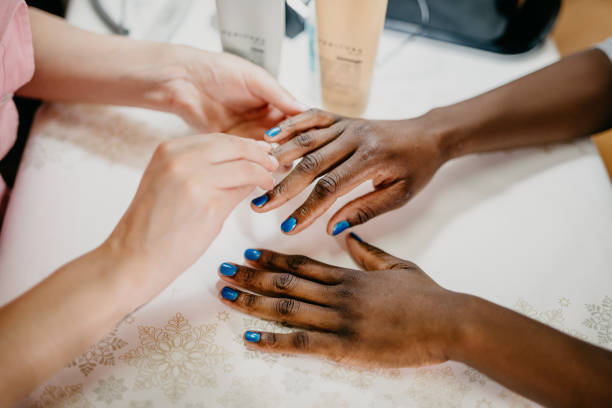 African ethnicity woman at spa receiving manicure from professional beautician Young african ethnicity woman having nail manicure at beauty spa salon. Close up on african woman's hands being nailpolished. nail salon stock pictures, royalty-free photos & images