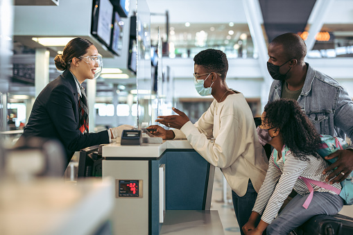 Passengers standing at check-in counter with airport staff during pandemic. African family in covid-19 outbreak at check-in desk of airport.