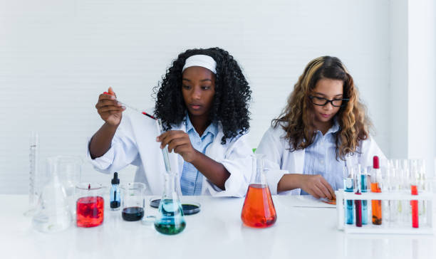 African girl students and Caucasian friends learning experiment research biology and chemical with colorful liquid in tube and beaker in laboratory room at school. stock photo