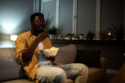 African man sitting at home in his room, watching horror movies