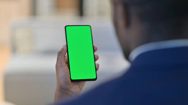 African Man using Smartphone with Chroma Screen Rear View of African American Man using Smartphone with Chroma Screen smart phone green background stock pictures, royalty-free photos & images