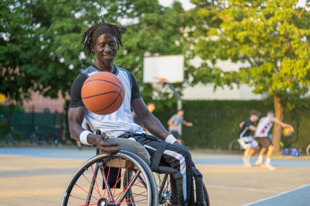 hombre africano con una discapacidad causada por la polio jugando al baloncesto, atleta campeón con discapacidad en una silla de ruedas, concepto de determinación y dureza mental - polio fotografías e imágenes de stock