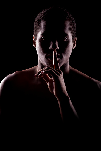 african man with the face in the shadow holding finger on lips