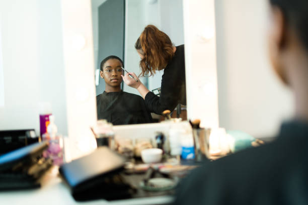 African model having make up applied backstage reflected in vanity mirror stock photo