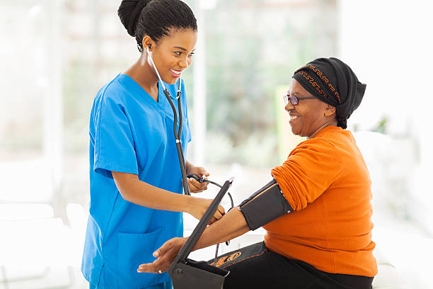 african nurse checking senior patient's blood pressure stock photo