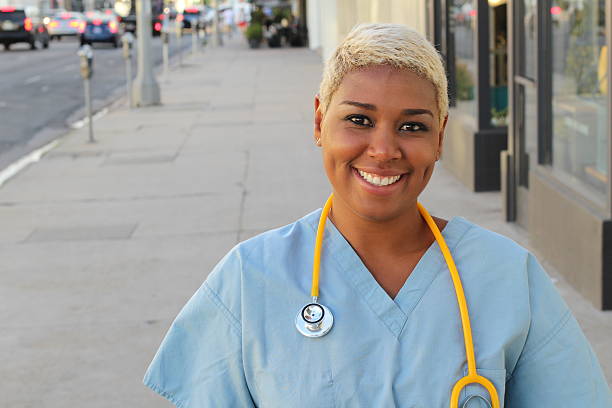 African nurse standing in the city streets Young happy afro american nurse standing outside of the hospital in the city streets. Smiling, looking at camera. nurse face stock pictures, royalty-free photos & images