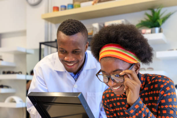 African optician explaining and selling eyeglasses to young woman girl customer in optical shop store. Eyecare concept. stock photo