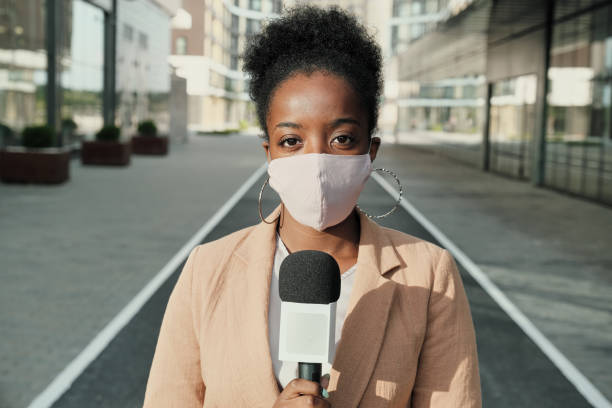 African reporter in mask Portrait of African young reporter in protective mask holding microphone and looking at camera while standing in the city journalism stock pictures, royalty-free photos & images