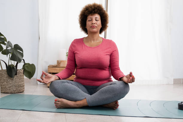 African senior woman doing pranayama breath exercises during yoga session at home - Focus on face stock photo