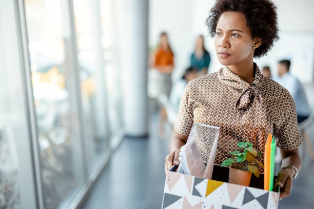 African Woman Getting Fired From Work Mature african woman getting fired from work. Female walks through the office, carrying box with personal belongings. Business, firing and job loss concept quitting a job photos stock pictures, royalty-free photos & images