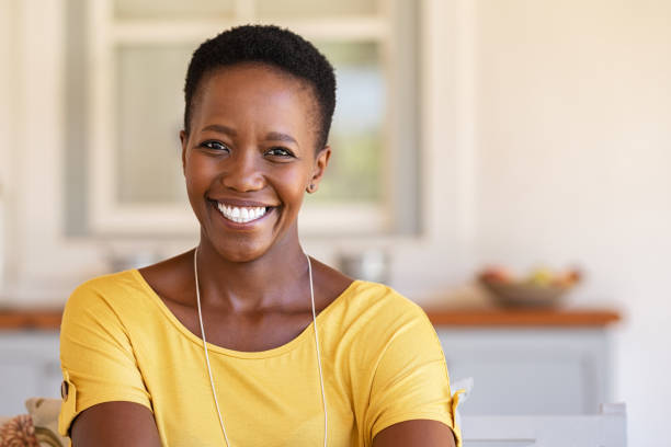 African woman looking at camera Mature happy woman smiling and looking at camera. Portrait of african american woman in casual clothing and curly short hair relaxing at home.  Portrait of successful black lady with copy space. mature women stock pictures, royalty-free photos & images