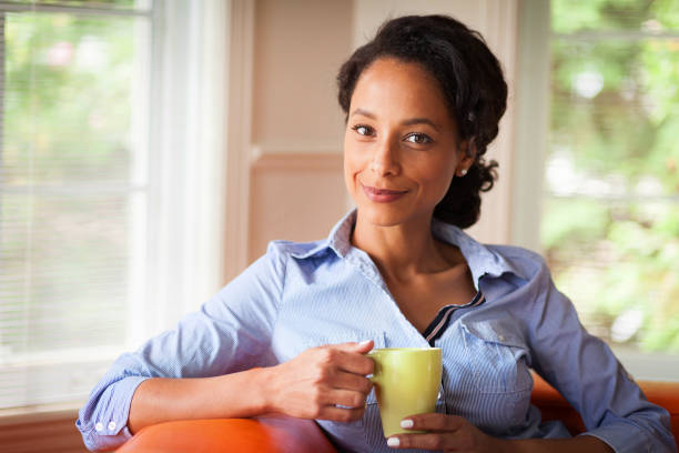 African Woman sitting on her sofa in her living room holding a cup . She relaxing . African Woman sitting on her sofa in her living room holding a cup . She relaxing . beautiful haitian women stock pictures, royalty-free photos & images