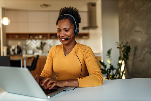 Smiling woman, working online, using earphones and laptop.