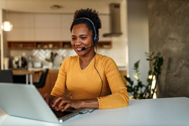African woman talking with someone over the laptop. Smiling woman, working online, using earphones and laptop. headset woman customer service stock pictures, royalty-free photos & images