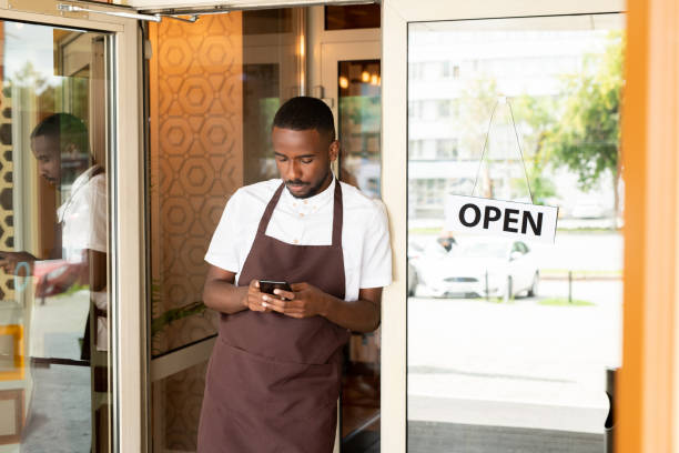 African young waiter with smartphone scrolling through new orders of clients stock photo