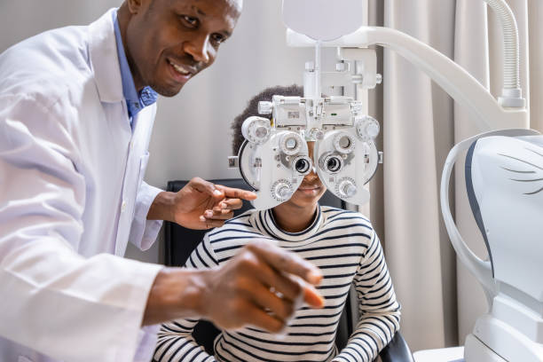 African young woman girl doing eye test checking examination with male man optometrist using phoropter in clinic or optical shop. Eyecare concept. stock photo