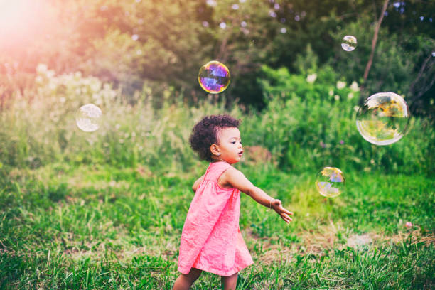 African-American baby girl playing with soap bubbles in the park stock photo