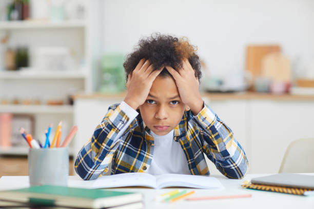 African-American Boy Studying at Home Portrait of cute African-American boy sitting at desk and looking at camera while struggling to finish homework, copy space banging your head against a wall stock pictures, royalty-free photos & images