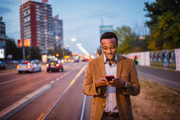 homme d’affaires afro-américain sur un voyage d’affaires utilisant le téléphone portable - night lugage photos et images de collection