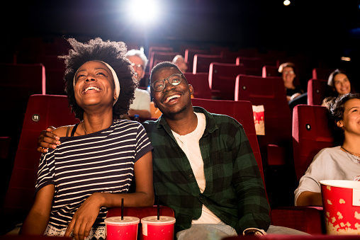 African-American couple watching a comedy movie at the cinema and enjoying.