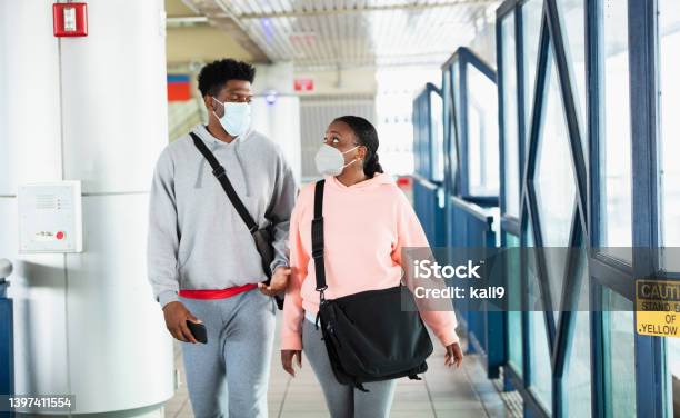 African-American couple on train platform wearing masks