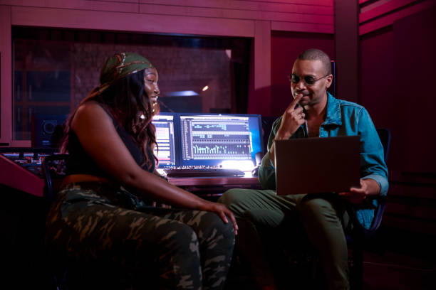 African-american female artist working with male music producer on laptop in music studio African-american female artist working on song track with male music producer on laptop in professional music studio producer stock pictures, royalty-free photos & images