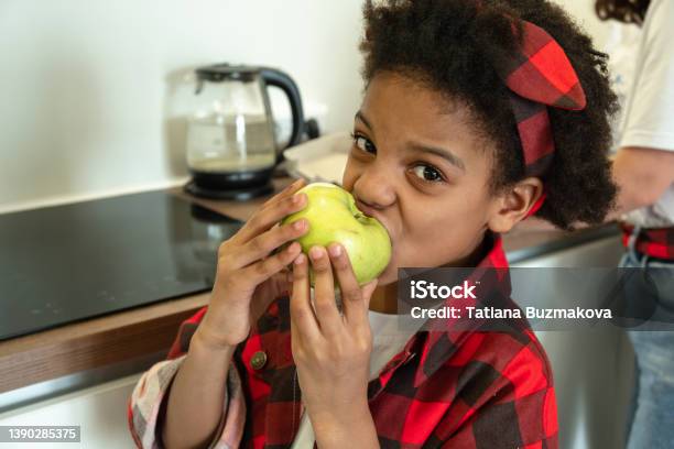 African-American girl eating an apple in the kitchen.Diverse people.Healthy eating.