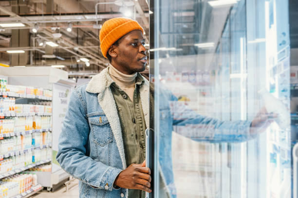African-American guy takes milk from fridge in supermarket stock photo