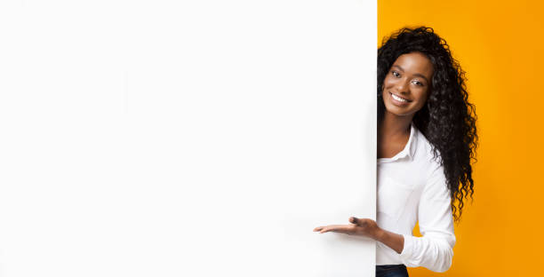 African-american man pointing at white blank board Awesome promo. Smiling african american woman presenting something on white blank board with empty space, panorama pointing stock pictures, royalty-free photos & images