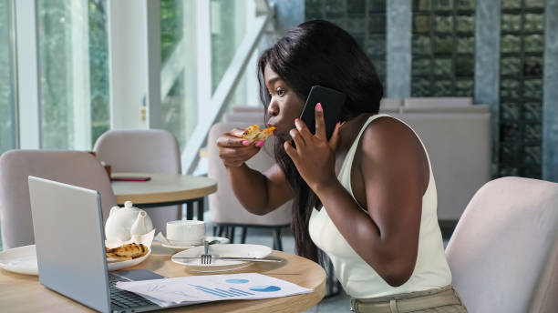 African-American manager talks on phone biting pizza in cafe stock photo